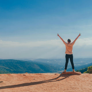 A girl stands at the top of a mountain, celebrating her achievement.